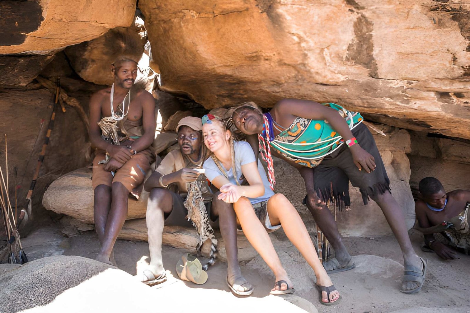 Hadzabe tribe members resting near a rocky outcrop, sharing a moment with visitors.