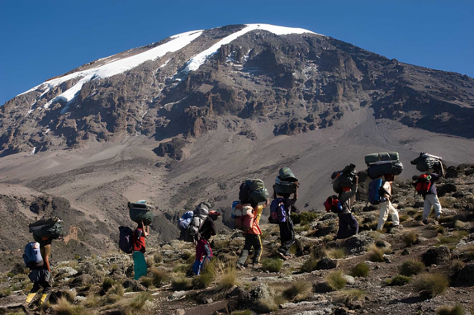 A group of trekkers with backpacks navigating a rocky mountain trail along a steep slope.